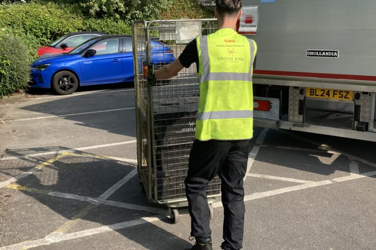 Member of GXO staff wearing a high vis GXO top pushing a trolley to the back of a lorry