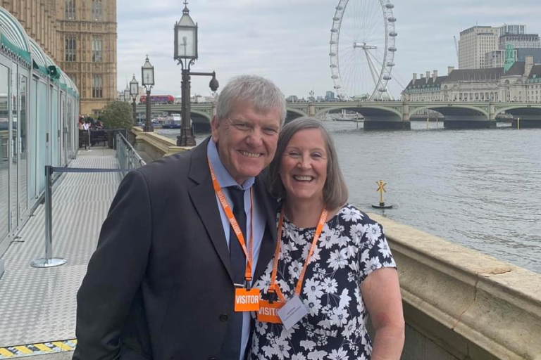 Ged and Julie standing o the riverside terrace at the Houses of Parliament