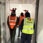 Photo shows several people walking through a door with their backs to the camera, they are all wearing hi vis vests with the word 'Garic' printed on the back and they are also all wearing antlers