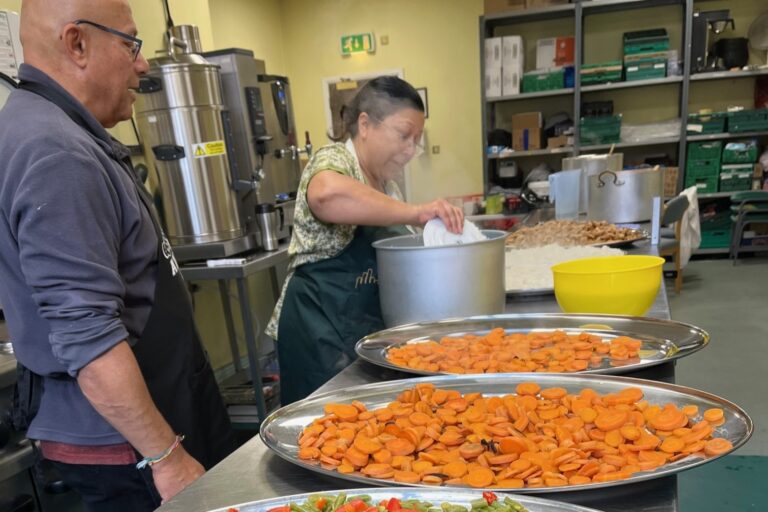 Tameside Meals Project cooking in progress at Hyde Town Hall Image shows platters filled with cooked vegetables and two volunteers making food