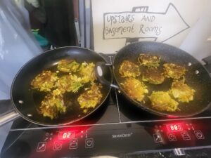 Close up of two frying pans each on the hob with cauliflower bhajis cooking in them