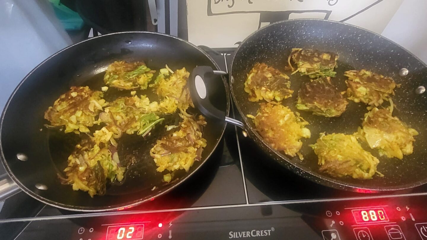 Close up of two frying pans each on the hob with cauliflower bhajis cooking in them