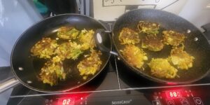 two frying pans on the hob with cauliflower bhajis cooking