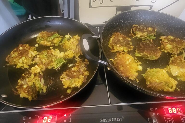 Close up of two frying pans each on the hob with cauliflower bhajis cooking in them