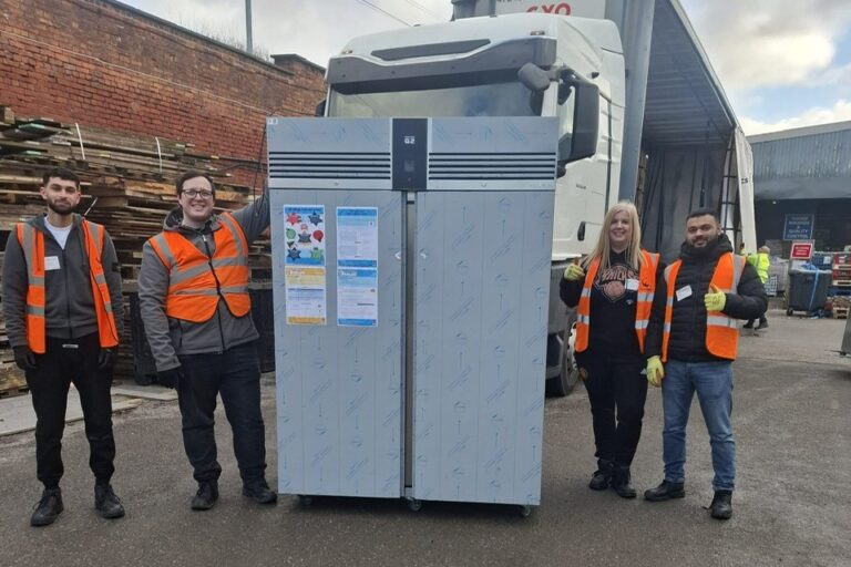 photo shows large fridge standing in the goods yard with four corporate volunteers standing alongside smiling at the camera with their thumbs up