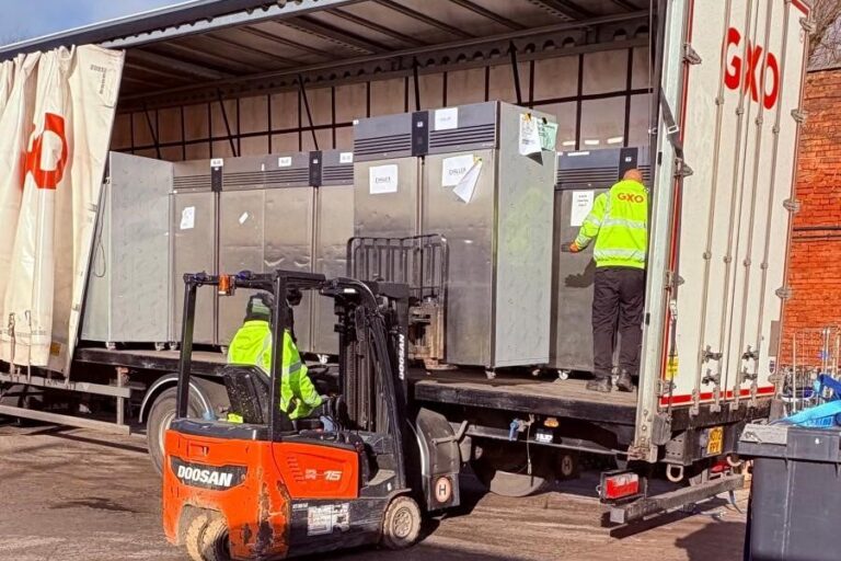 Photo shows a forklift taking a large fridge off the back of a large lorry