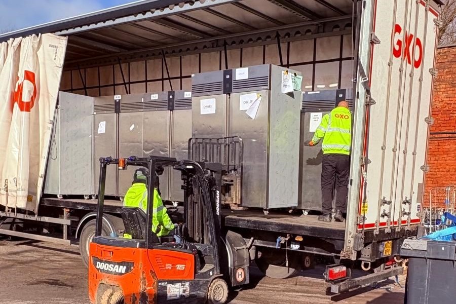 Photo shows a forklift taking a large fridge off the back of a large lorry