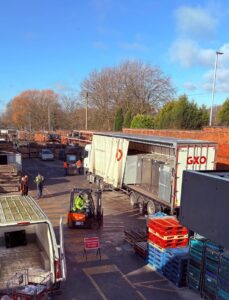 Photo shows view of the FareShare Greater Manchester goods yard taken from above. It shows a large GXO lorry filled with fridges being off loaded by a forklift truck