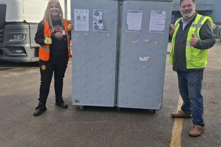 Photo shows a large fridge standing in the FareShare Greater Manchester goods yard with two people smiling at the camera with their thumbs up