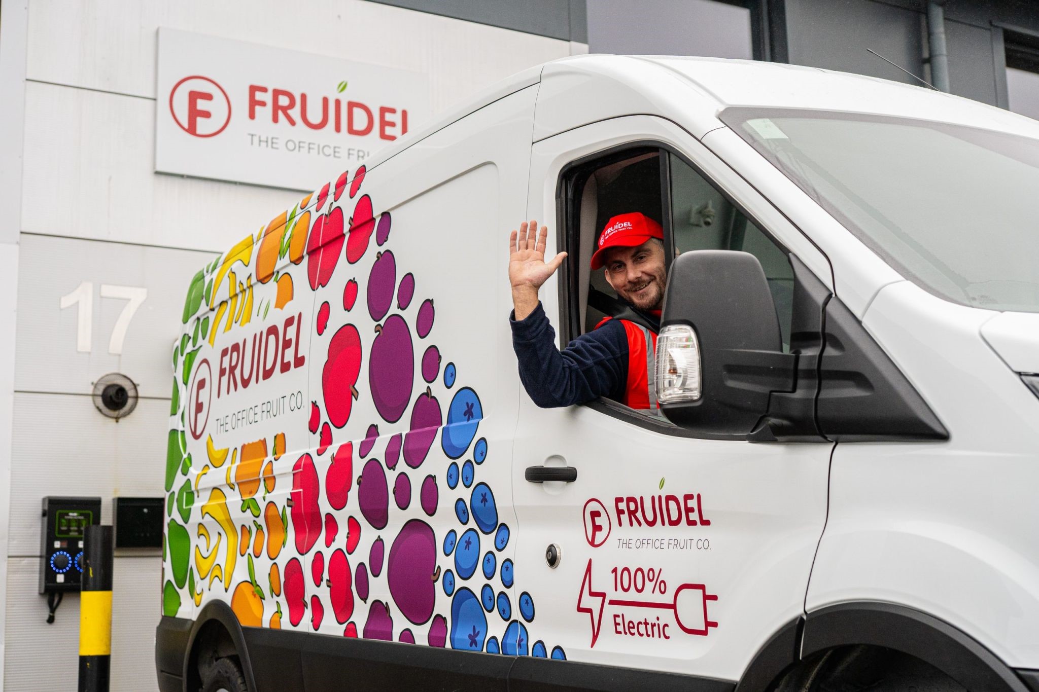 Image shows a Fruidel liveried vehicle parked in front of Fruidel HQ. The driver is leaning out of the van window waving and smiling at the camera
