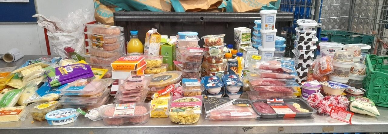 Image shows an industrial catering table covered in items of food which have been donated to FareShare Greater Manchester
