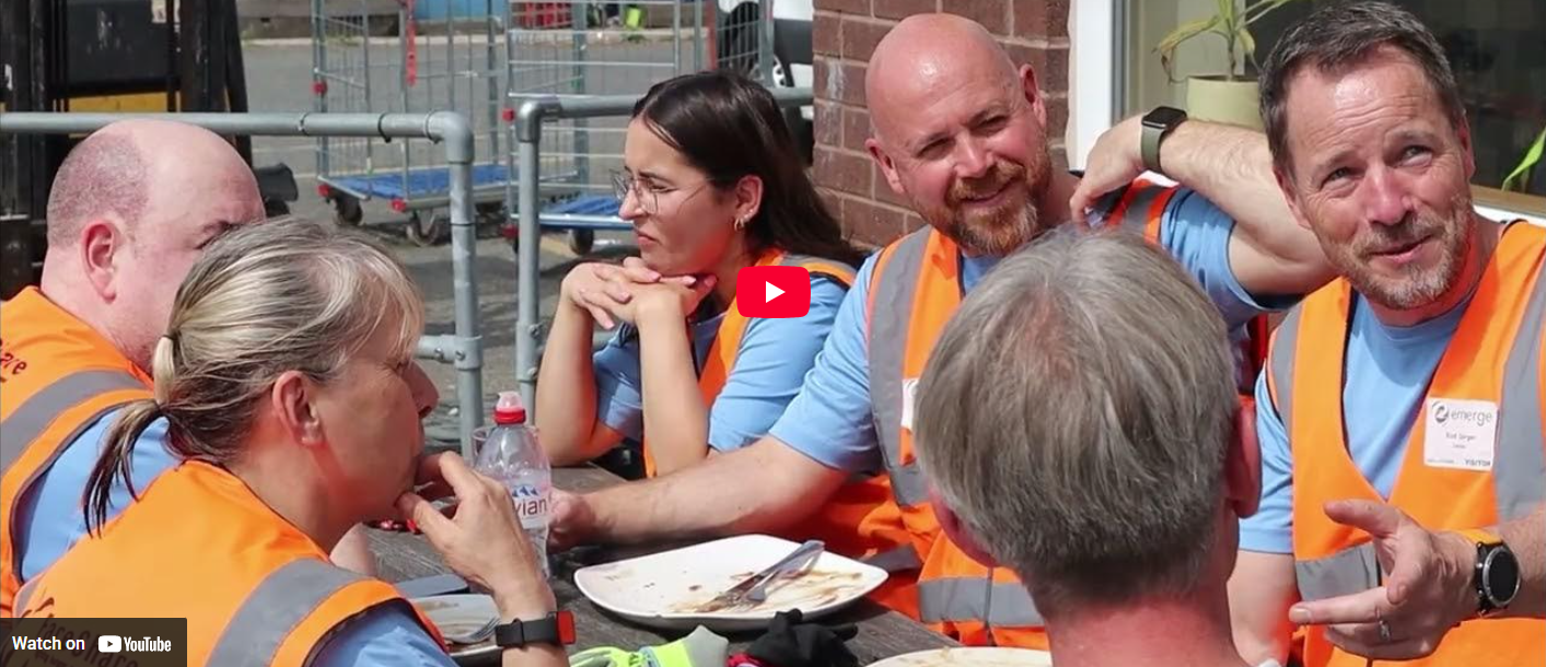 Image shows a team of corporate volunteers sitting outside FareShare Greater Manchester chatting over lunch